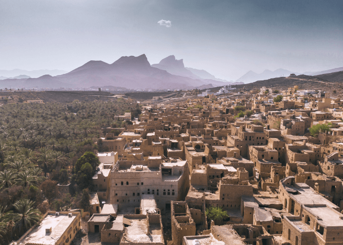 ancient-omani-village-aerial-mountains-pink-jinn.jpg Aerial view of a historic Omani mud-brick village surrounded by date palms and dramatic mountain peaks